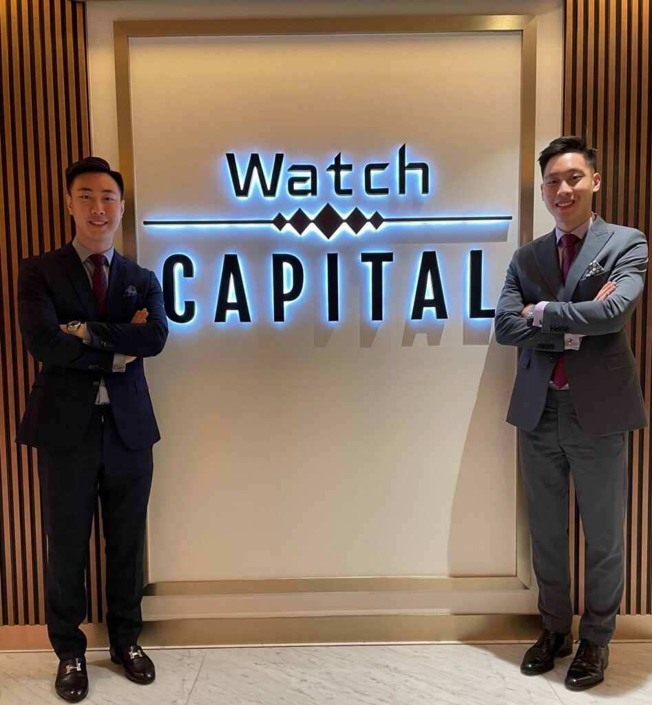 Two Watch Capital team members in suits standing beside the illuminated Watch Capital signage
