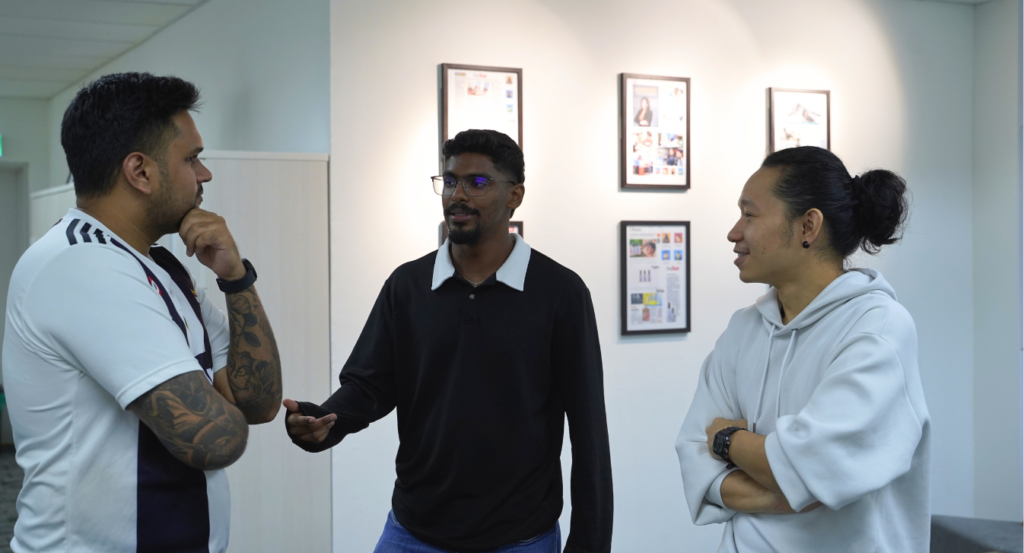 Three colleagues talking in an office hallway beside framed press clippings