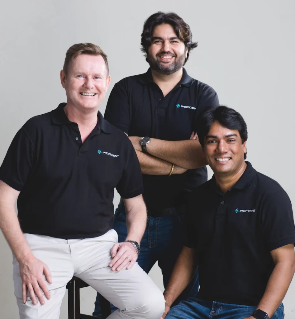 Three Proficient team members in branded polo shirts posing together in a studio portrait