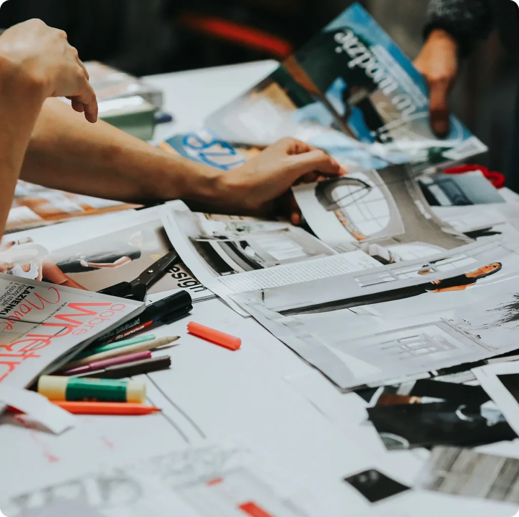 Hands arranging magazine clippings and design materials on a brand marketing moodboard table