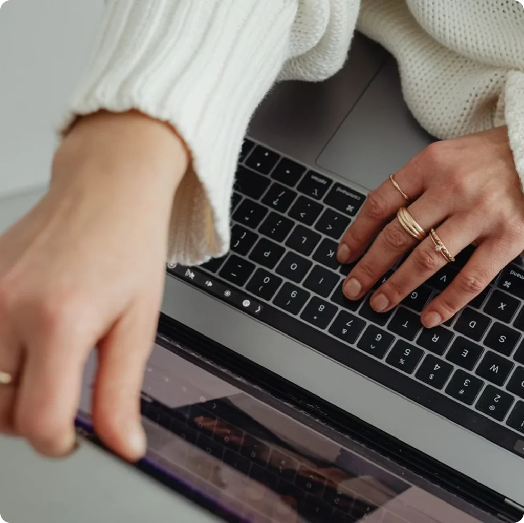 Woman in a cream sweater typing on a MacBook, illustrating digital solutions work