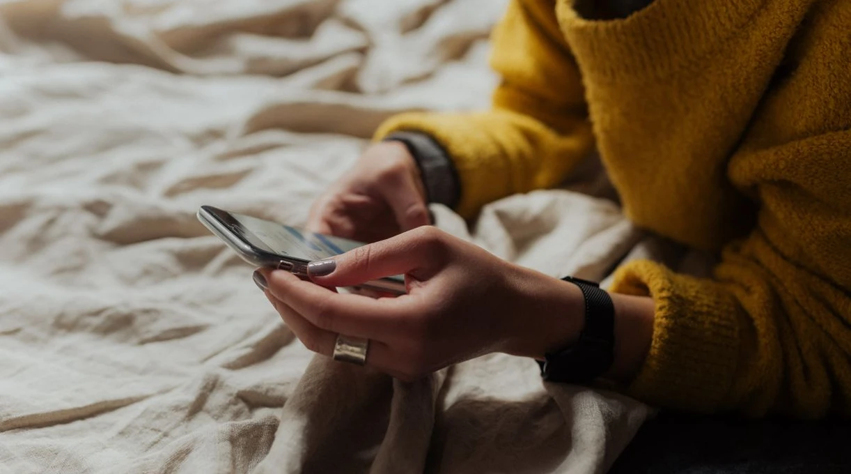 Woman in a yellow sweater scrolling social media on her smartphone