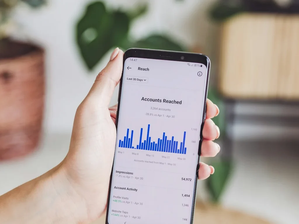 Hand holding a smartphone showing Instagram Reach analytics and account engagement charts
