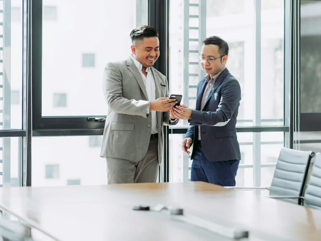 Two businessmen in suits reviewing a phone in a Singapore boardroom
