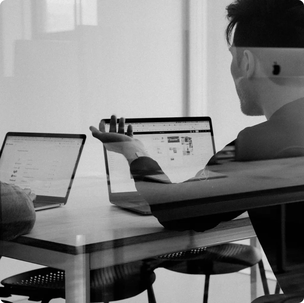 Black and white photo of two colleagues reviewing analytics on laptops across a meeting table