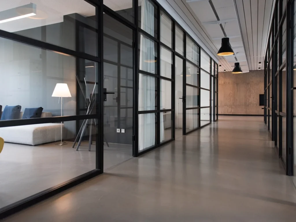 Modern office corridor with black-framed glass partitions and polished concrete floor