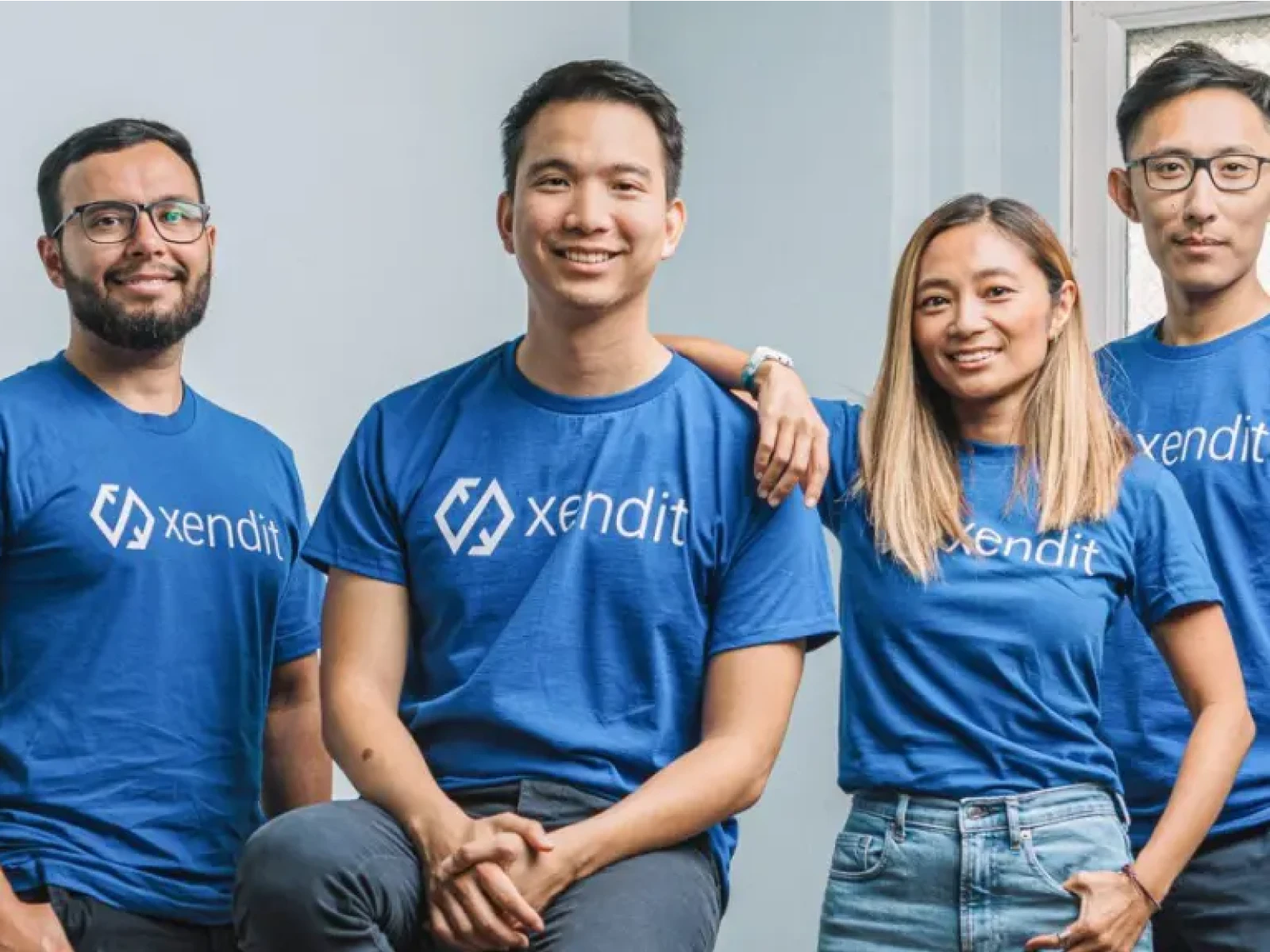 Four Xendit team members in blue branded t-shirts smiling together